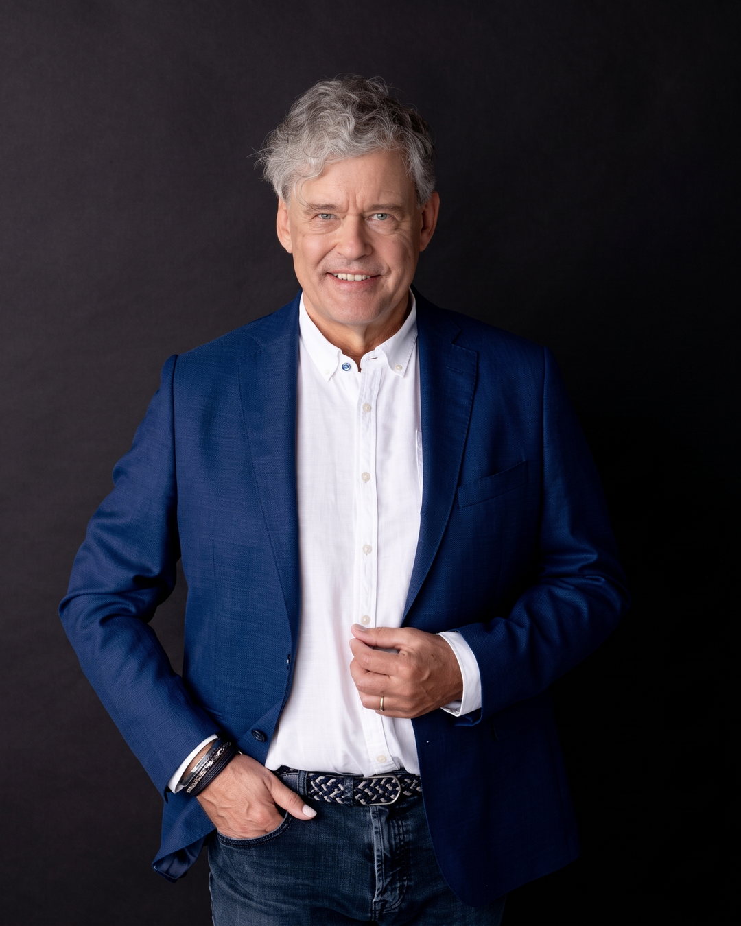Charles Groenhuijsen, staand portret in blauw colbert tegen een donkere achtergrond